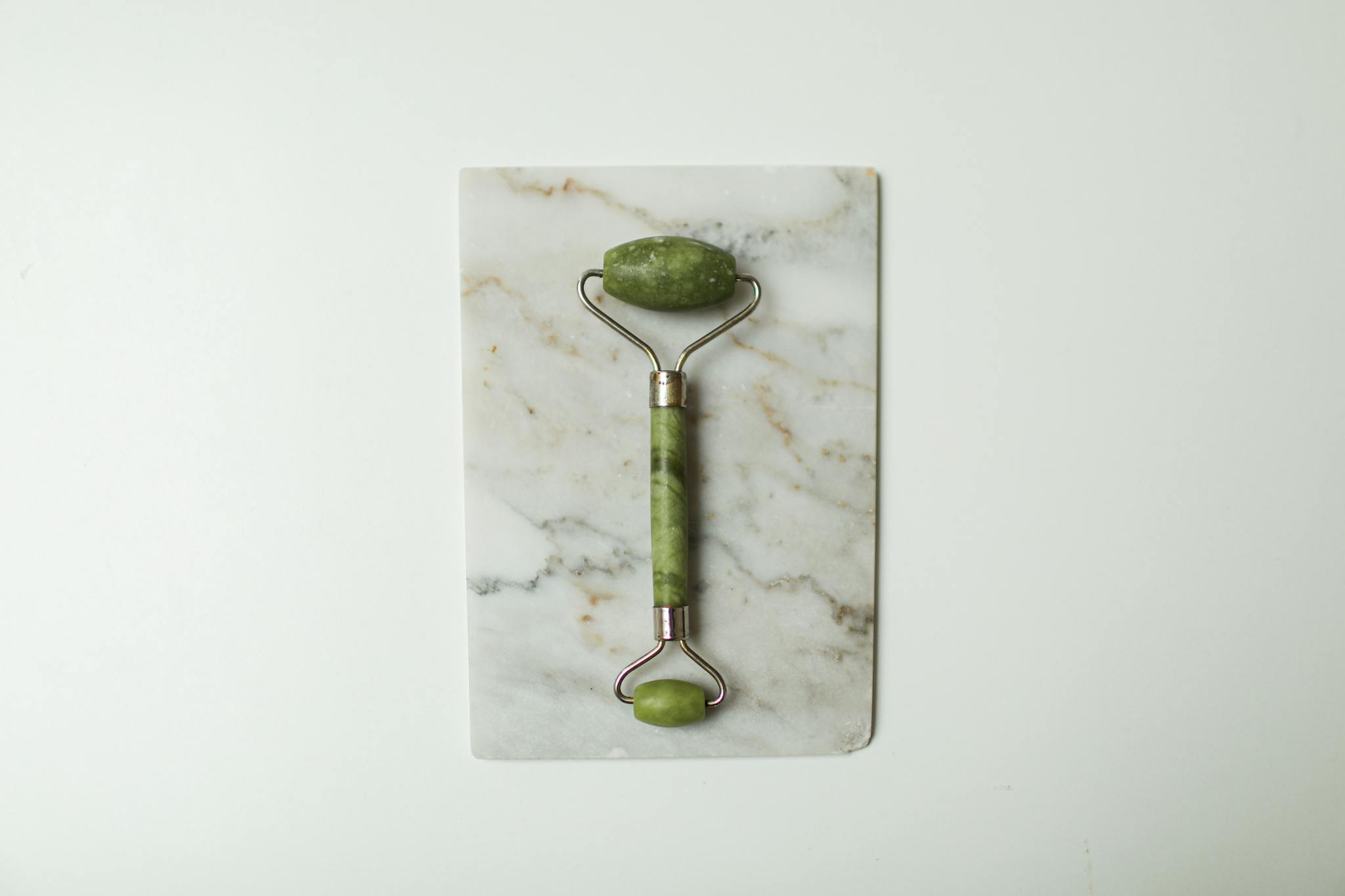 Close-up of a jade face roller on a marble slab, ideal for skincare and facial massage routines.